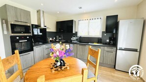 A modern kitchen with grey cabinets, a wooden dining table, and a vase of flowers. - Gîte le Bouirou - LES MARTYS (LES MARTYS)