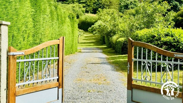 A gravel pathway leading through a well-maintained garden with neatly trimmed hedges and a wooden gate with metal bars. - Gîte le Bouirou - LES MARTYS (LES MARTYS)
