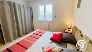 A bedroom with a bed, two pillows, a bedside table with a lamp, a window, and curtains. - Gîte le Bouirou - LES MARTYS (LES MARTYS)