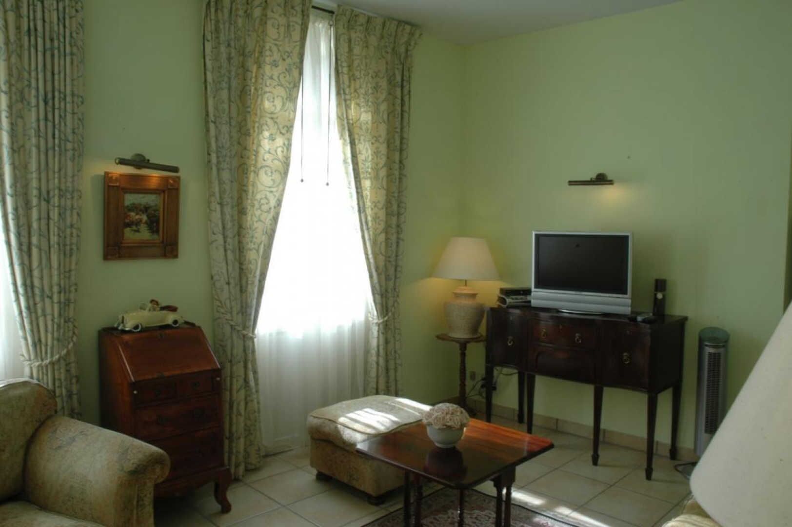Un salon comprenant un canapé, une petite table avec une lampe, un téléviseur posé sur un meuble et une armoire.