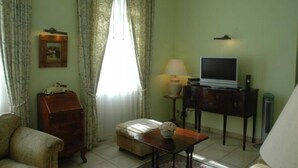 Een woonkamer met een bank, een tafeltje met een lamp, een televisie op een dressoir en een kast.