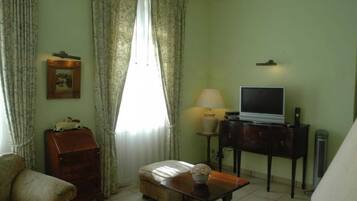 Un salon comprenant un canapé, une petite table avec une lampe, un téléviseur posé sur un meuble et une armoire.