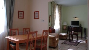 Een zithoek met een houten tafel en stoelen, een bank, een televisie en een lamp.