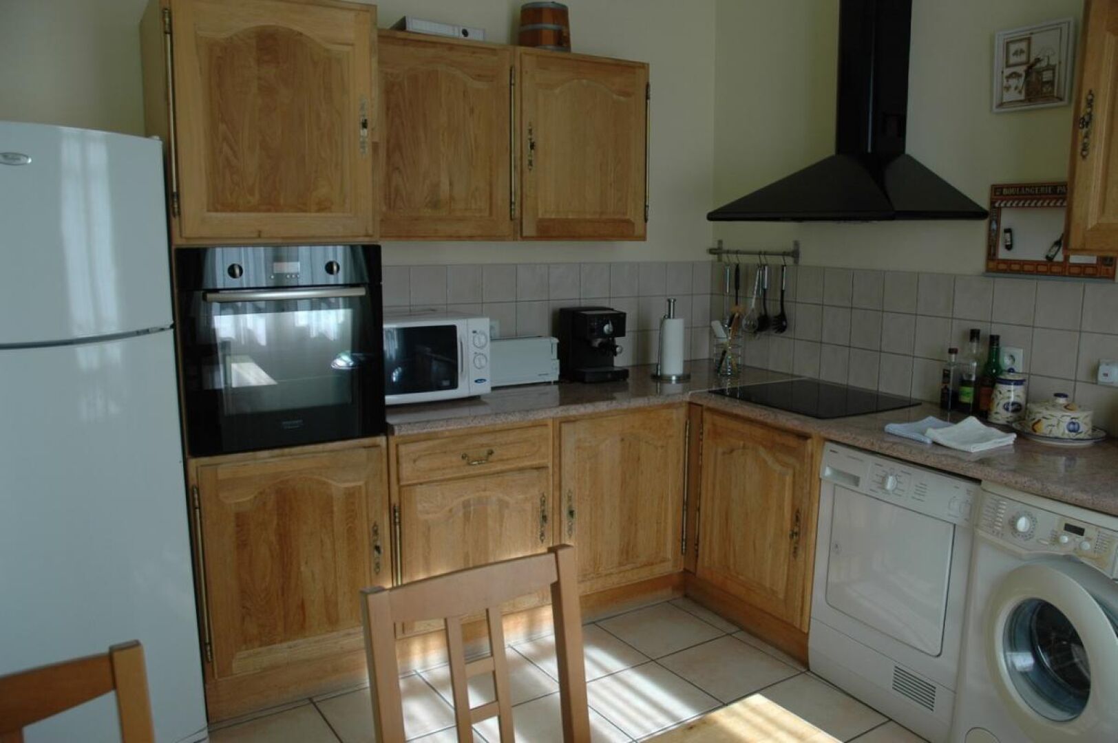 Une cuisine équipée de meubles en bois, d’un r éfrigérateur, d’un four, d’un four à micro-ondes, d’une machine à café, d’un évier et d’un lave-linge.