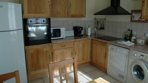 Een keuken met houten kastjes, een koelkast, een oven, een magnetron, een koffiezetapparaat, een spoelbak en een wasmachine.
