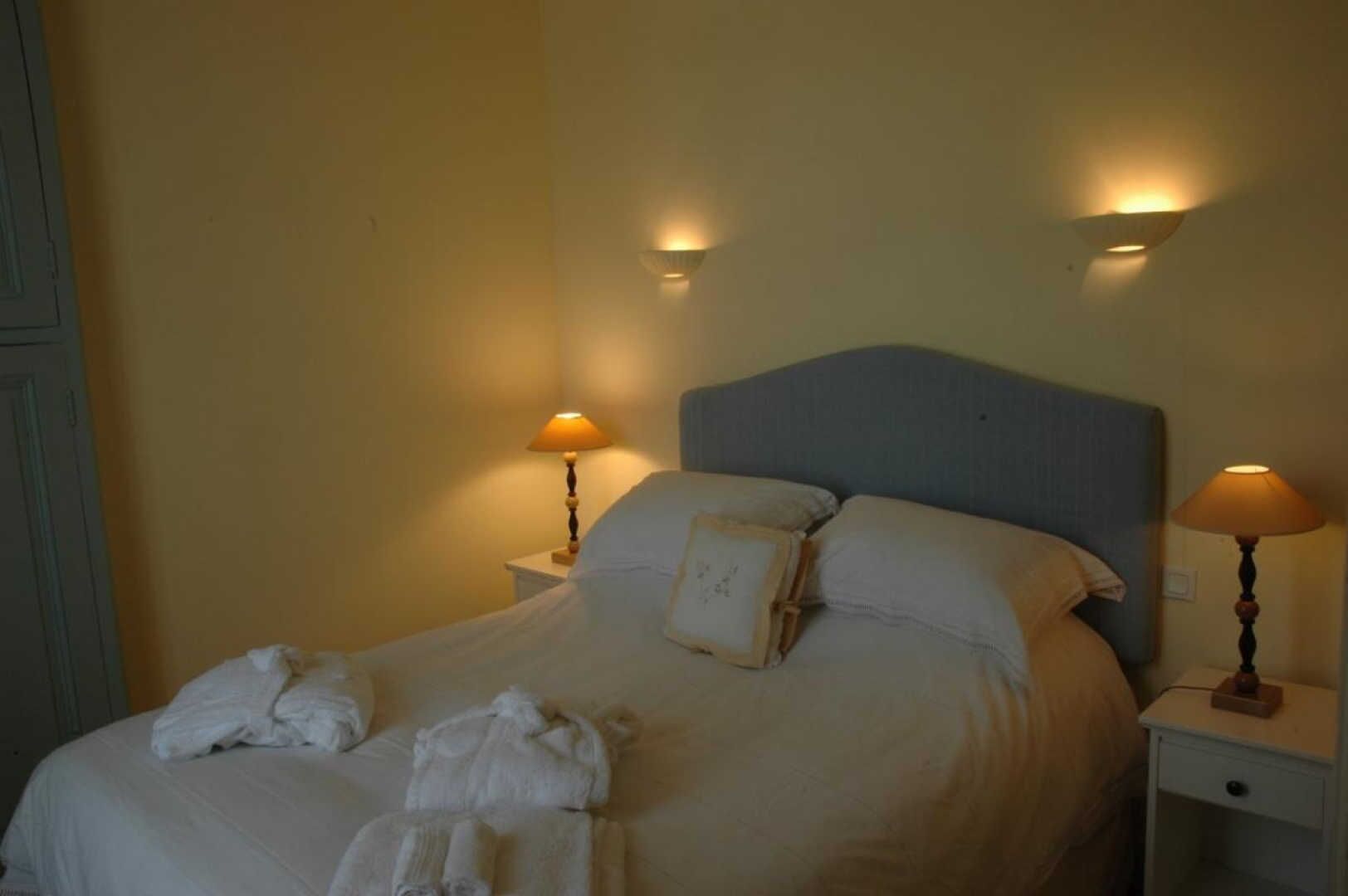 A neatly made bed with white linens and towels, two bedside lamps, and a headboard.