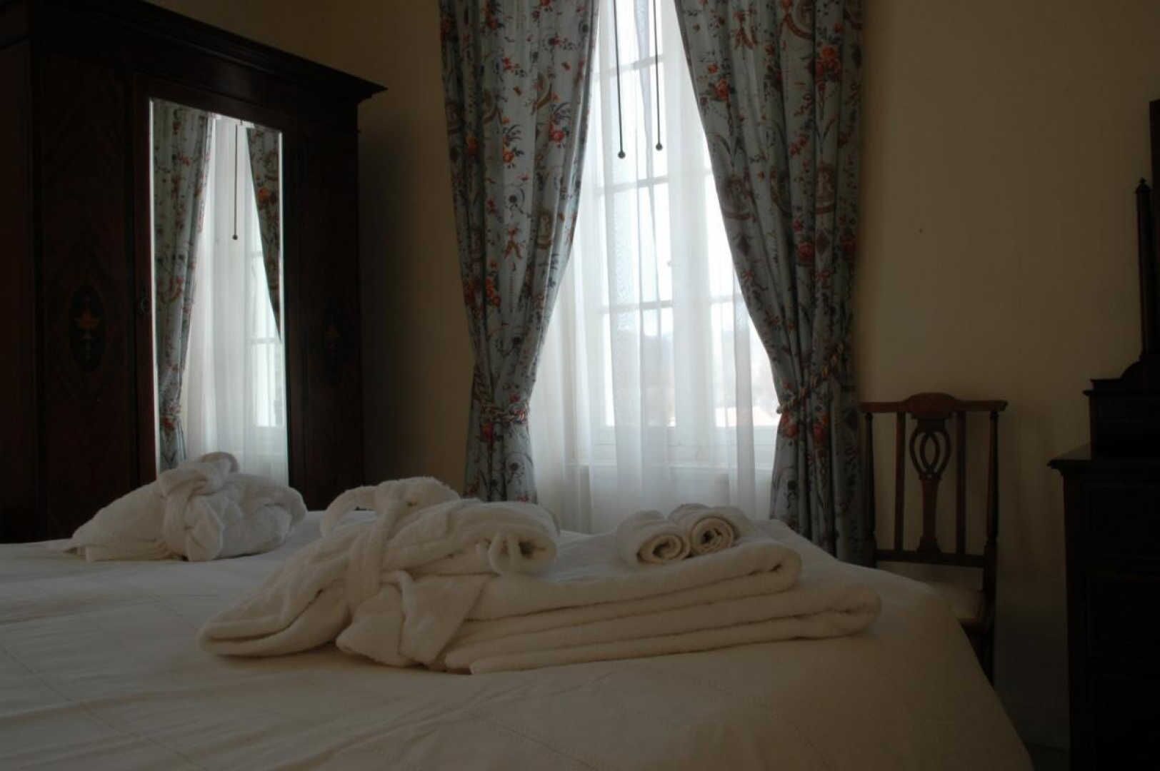 Une chambre d’hôtel avec un lit, deux fenêtres ornées de rideaux à motifs floraux et une tête de lit en bois.