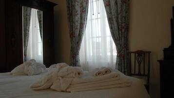 Une chambre d’hôtel avec un lit, deux fenêtres ornées de rideaux à motifs floraux et une tête de lit en bois.