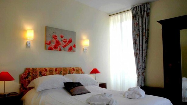 Een hotelkamer met een groot bed, twee nachtkastjes met lampen, een schilderij aan de muur en een raam met gordijnen.