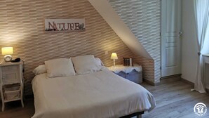 A bedroom with a sloped ceiling, a bed with white bedding, a nightstand with a lamp, and a wall-mounted sign that reads "NATURE".