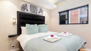 Un dormitorio moderno con una cama grande, almohadas mullidas, un cuadro con motivos de cebra y una ventana con vista a un edificio.