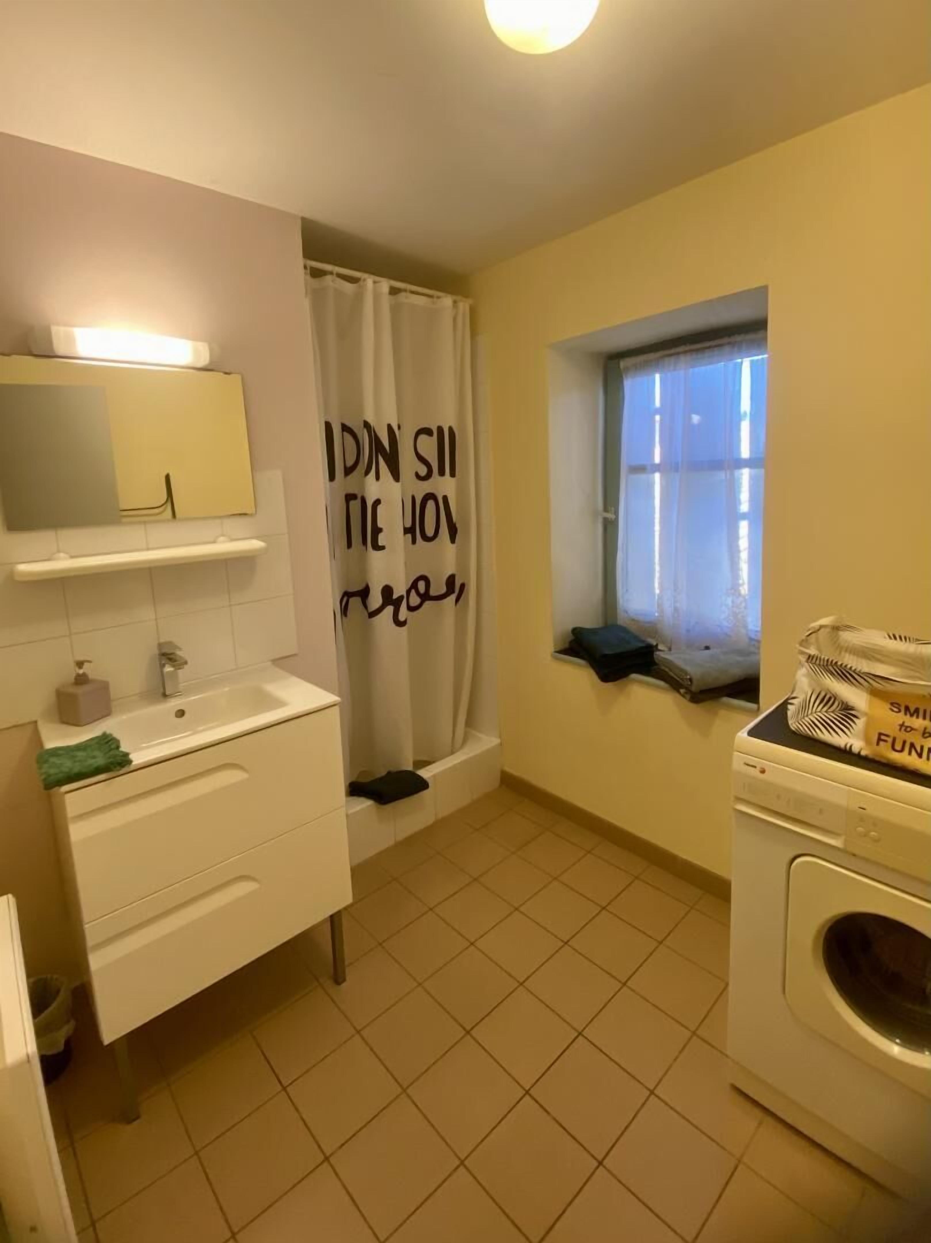 Un bagno con lavandino bianco, specchio, tenda della doccia e una finestra.