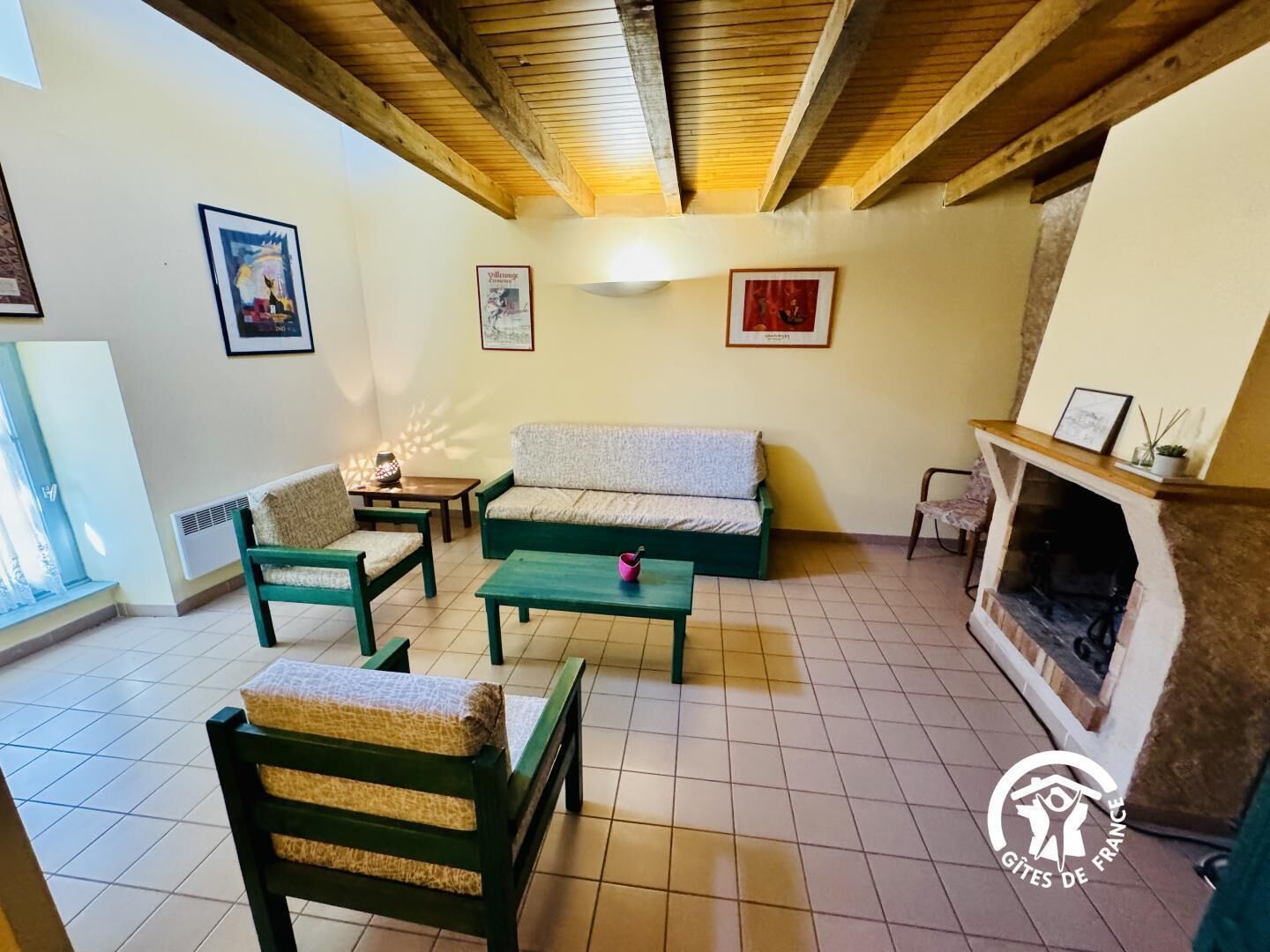 Een gezellige woonkamer met een groene bank, twee groene fauteuils, een kleine tafel en een open haard.