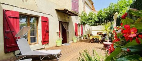 Une terrasse en bois avec deux chaises longues, une table et des plantes en pot.