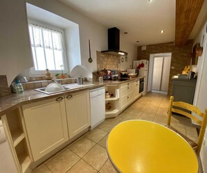 A modern kitchen with white cabinets, a yellow chair, and a window with curtains.