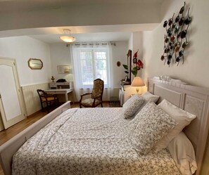 A bedroom with a bed, a chair, a desk, and a window with curtains.