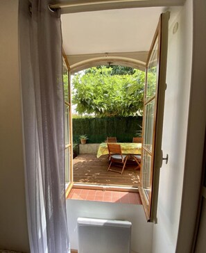 A room with a sliding glass door leading to an outdoor patio with a table and chairs, a potted plant, and a green hedge.