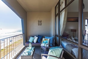 A balcony with wicker furniture, a view of the beach, and a sign with a beach-related message.