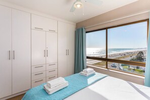Une chambre d’hôtel avec un lit, une grande fenêtre donnant sur la plage et une armoire avec de nombreux tiroirs.