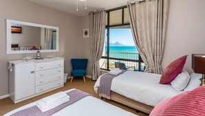 A bedroom with a bed, a dresser, a chair, and a window with a view. - Beachfront 3BR | Ocean Views & BBQ Balcony by CTHA (Cape Town)