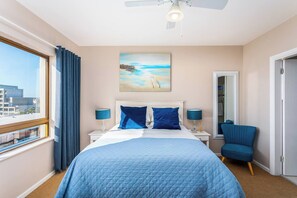 Una camera d'albergo con un letto, una poltrona, un quadro, una finestra e una ventola a soffitto.