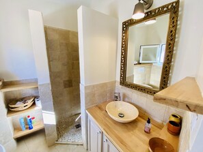 A bathroom with a beige sink, a wooden vanity, a large mirror with an ornate frame, and a shower area with stone tiles.