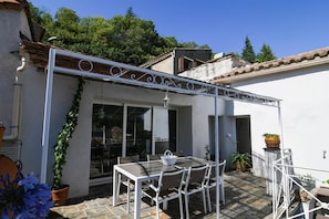Eine Terrasse mit Tisch und Stühlen, umgeben von Topfpflanzen und einer weißen Pergola.