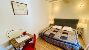 Un dormitori amb un llit, petites làmpades al costat, una taula de treball amb una cadira, i un certificat emmarcat a la paret.