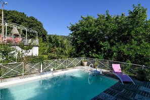 A swimming pool with a wooden deck, surrounded by a white fence and lush greenery.