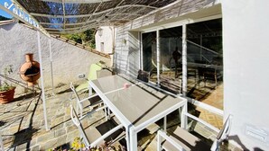 Un pati exterior amb taula i cadires, una pèrgola i vista cap a l'interior.