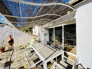 Een terras buiten met een tafel, stoelen, een pergola en uitzicht op het interieur.