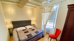 A bedroom with a bed, two bedside lamps, a red chair, and a view of the outdoors. - La Maison du Berger - CAUNES MINERVOIS (CAUNES MINERVOIS)
