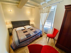 A bedroom with a bed, two bedside lamps, a red chair, and a view of the outdoors.