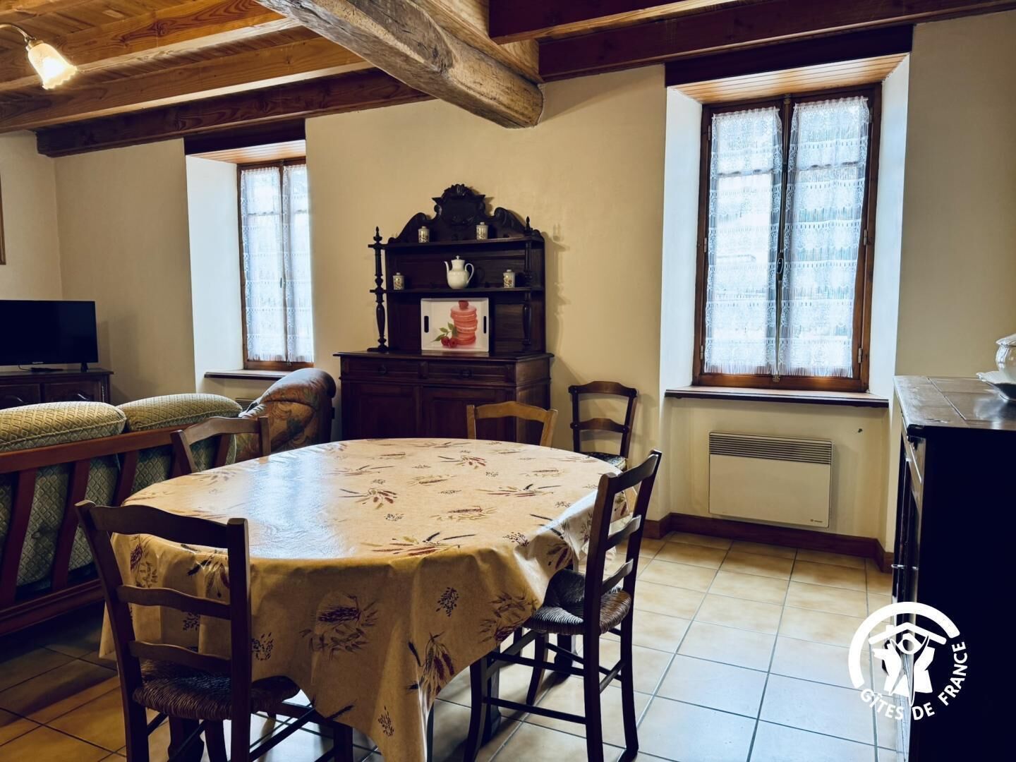 Un coin repas comprenant une table ronde, des chaises, un buffet en bois avec une théière et un téléviseur.