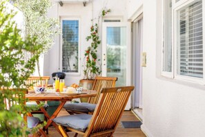 Een buiten eethoek met een houten tafel en stoelen, een bloempot en een glazen deur die leidt naar een overdekt terras.