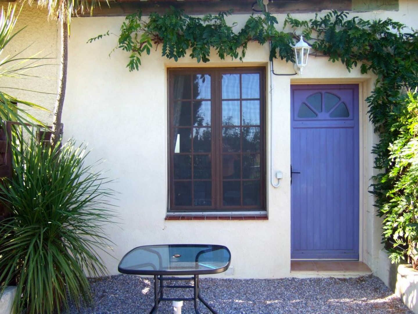 A house with a purple door, a window, and a small table in front.