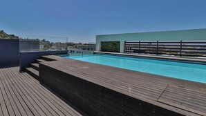 Une piscine sur le toit, dotée d’une terrasse en bois et offrant une vue sur le paysage urbain.