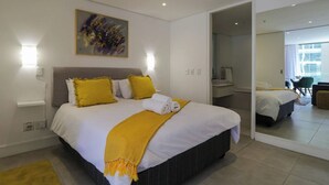 Une chambre d’hôtel moderne avec un grand lit, un tableau accroché au mur et une salle de bain visible à travers une porte ouverte.