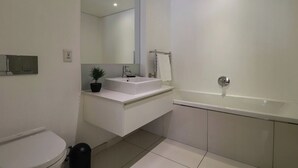 Une salle de bain moderne avec un lavabo blanc, un miroir, une baignoire et des toilettes.