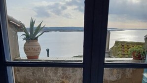 A view from a window overlooking a tiled patio with a potted plant and a view of the sea. - Nature Sauvage Méditerranée (BAGES)