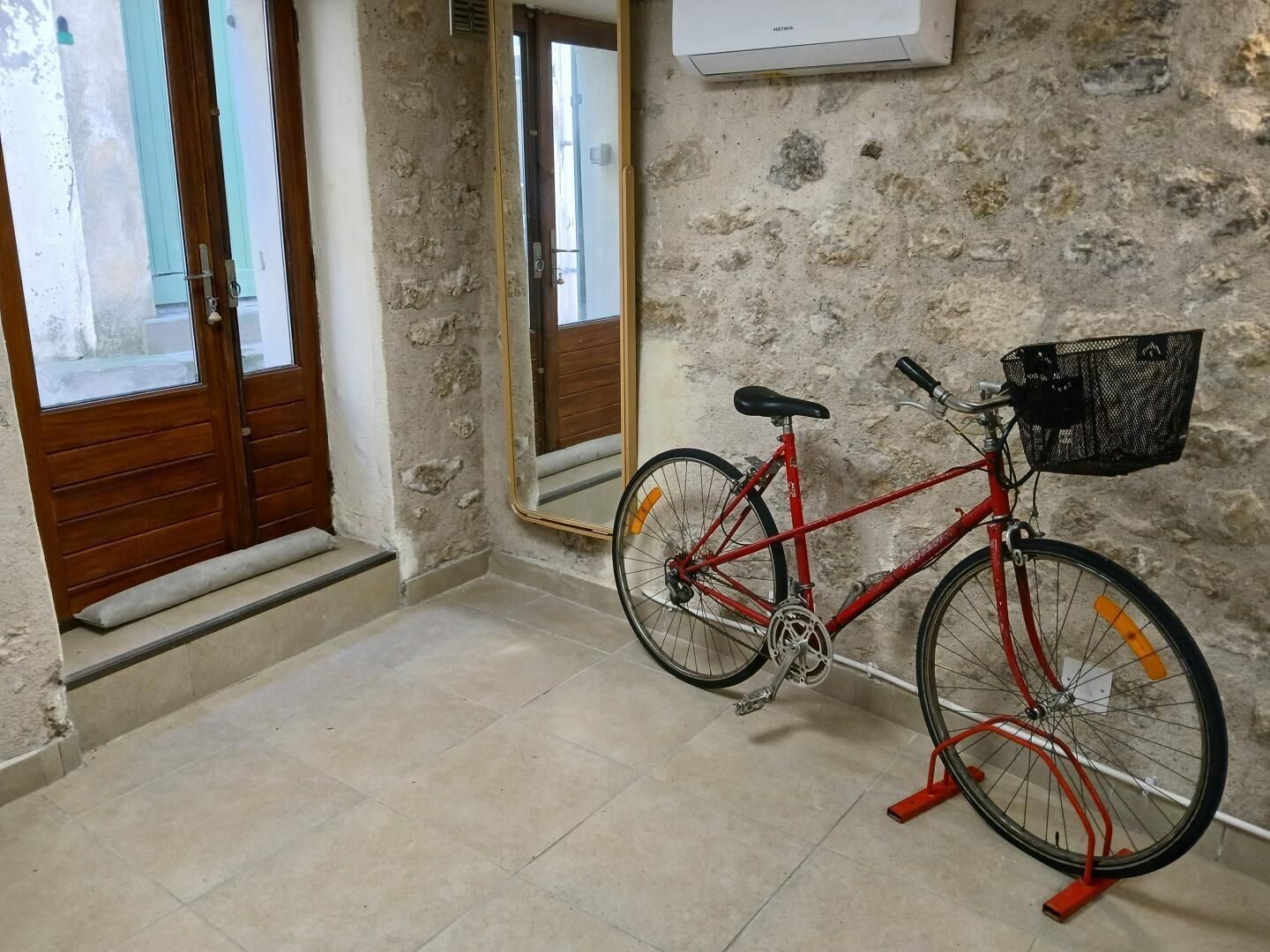 Ein Zimmer mit einem roten Fahrrad, einem Spiegel und einer Tür mit Holzrahmen.