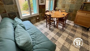 A cozy room with a green sofa, a wooden dining table with chairs, and a kitchen area with a wooden cabinet. - Nature Sauvage Méditerranée (BAGES)