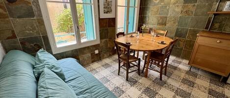 A cozy room with a green sofa, a wooden dining table with chairs, and a kitchen area with a wooden cabinet.