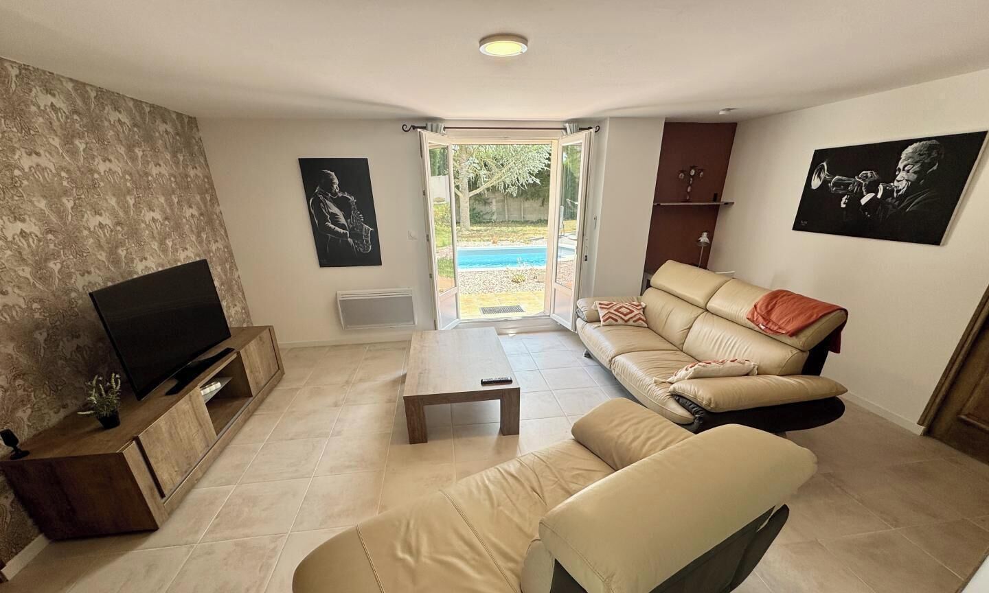 A living room with a sofa, a coffee table, a TV on a wooden stand, and a sliding glass door leading to a balcony.