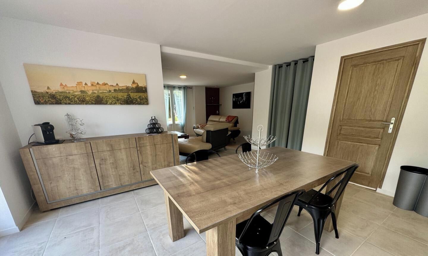 A modern living room with a wooden dining table, black chairs, a sofa, and a large window.