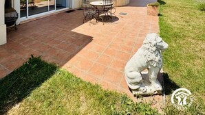 A two-story house with a curved roof, a patio with a table and chairs, and a statue of a lion.