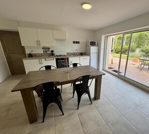 A modern kitchen with white cabinets, a dining table with chairs, and a large sliding glass door leading to an outdoor patio. - Les 3 Tours - 2 - ROULLENS (ROULLENS)
