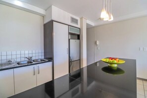 A modern kitchen with a black countertop, stainless steel appliances, and a yellow fruit bowl.