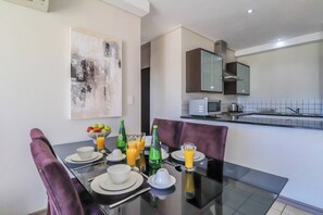 A dining area with a table set for two, a bowl of fruit, and glasses of orange juice. - Canal-side 2br, Balconies & Great location by ctha (Century City)