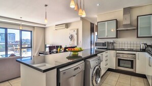 A modern kitchen with a dishwasher, washing machine, stove, and microwave. There is a large window providing a view of the city. - Canal-Side 2BR, Balconies & Great Location by CTHA (Century City)